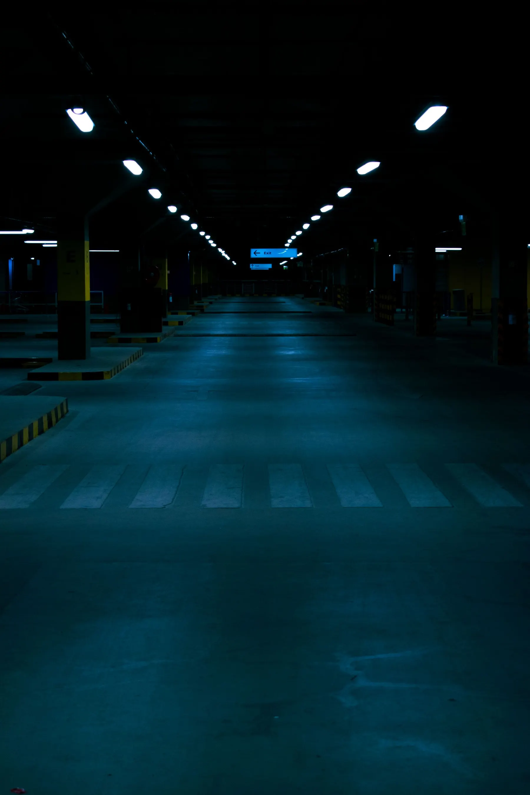 Empty parking structure glowing with blue light at night, lined with painted crosswalk stripes